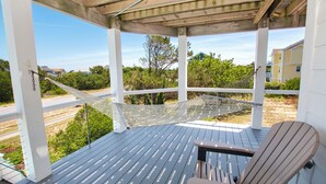 Eine überdachte Terrasse im Freien mit einer Hängematte, einem Holzstuhl und Blick auf Grünflächen und Gebäude.
