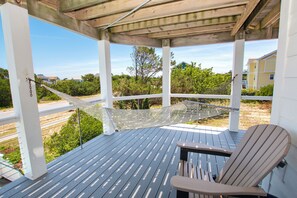 Eine überdachte Terrasse im Freien mit einer Hängematte, einem Holzstuhl und Blick auf Grünflächen und Gebäude.