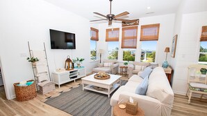 Ein modernes Wohnzimmer mit Deckenventilator, Flachbildfernseher, einer Couch, einem Couchtisch und Blick ins Freie.