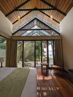 Un dormitorio con una cama grande, techo de madera y vistas a un área exterior con sillas y una mesa a través de puertas de vidrio.