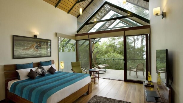 A bedroom with a large bed, a view of the outdoors, a balcony, and a TV. - Waterwoods Lodge Kabini (Heggadadevankote)