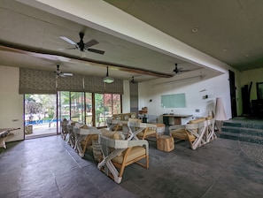 A spacious room with multiple wicker chairs, ceiling fans, a large window, and a television.