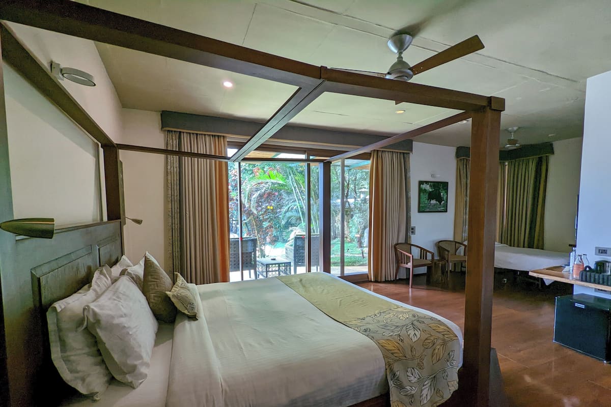 A bedroom with a large bed, a ceiling fan, and a view of the garden through the glass door.