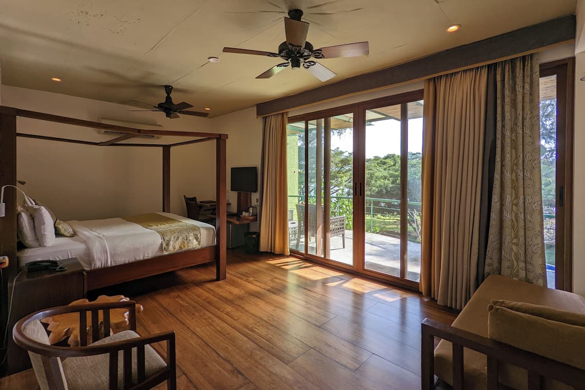 A four-poster bed, a ceiling fan, a television, and a balcony with curtains.