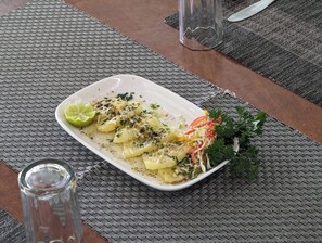 Une assiette rectangulaire blanche sur laquelle est servie une salade, le tout posé sur un set de table en fibres tressées.