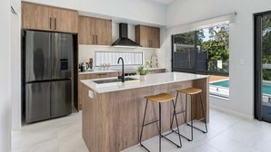 Una cucina moderna con isola centrale, elettrodomestici in acciaio inossidabile, mobili in legno e vista su una piscina.