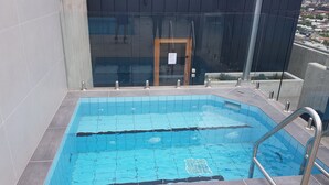 Ein Pool mit Glasumrandung, Metallgeländern und einer Tür zu einem überdachten Bereich.