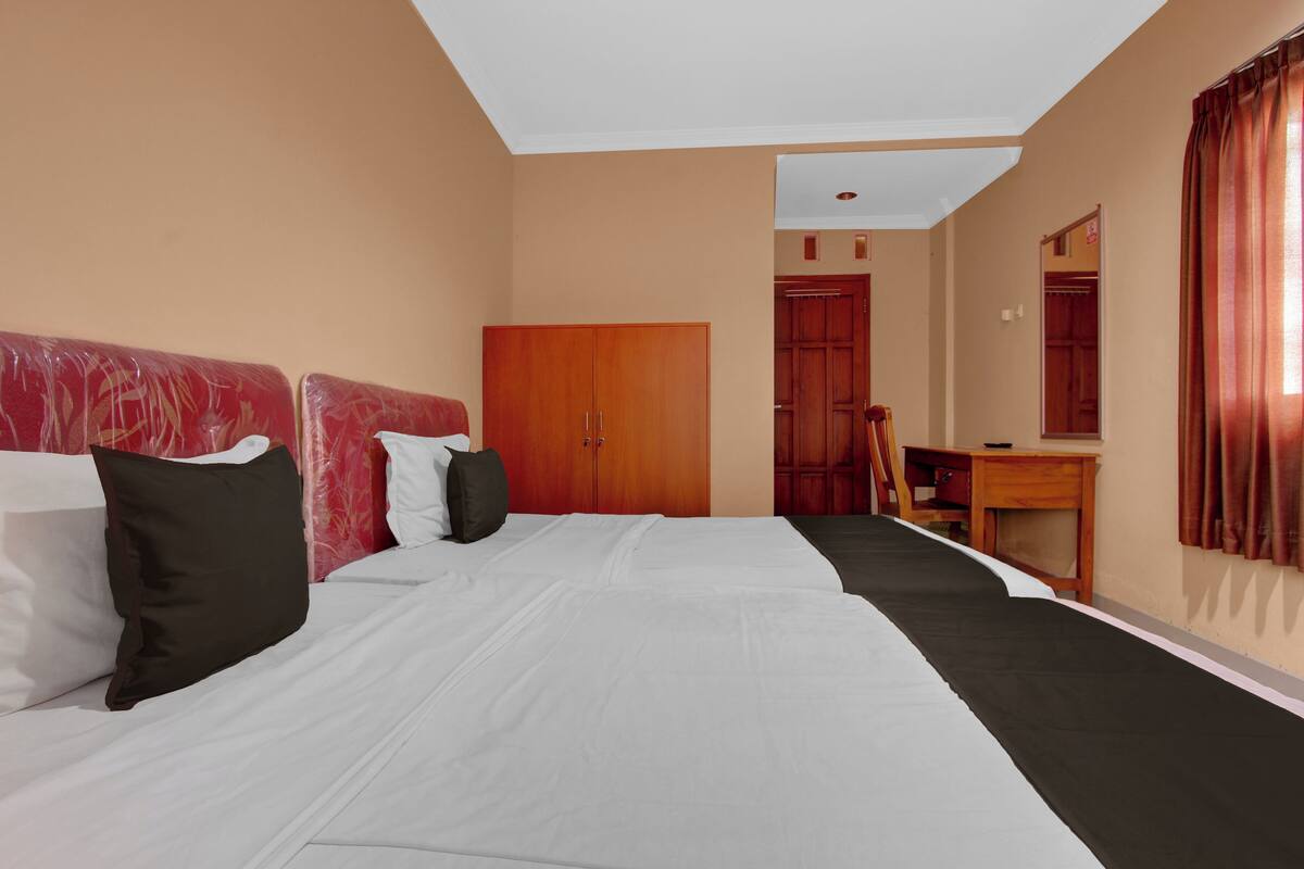 Quarto de hotel com cama, escrivaninha, guarda-roupa e espelho.