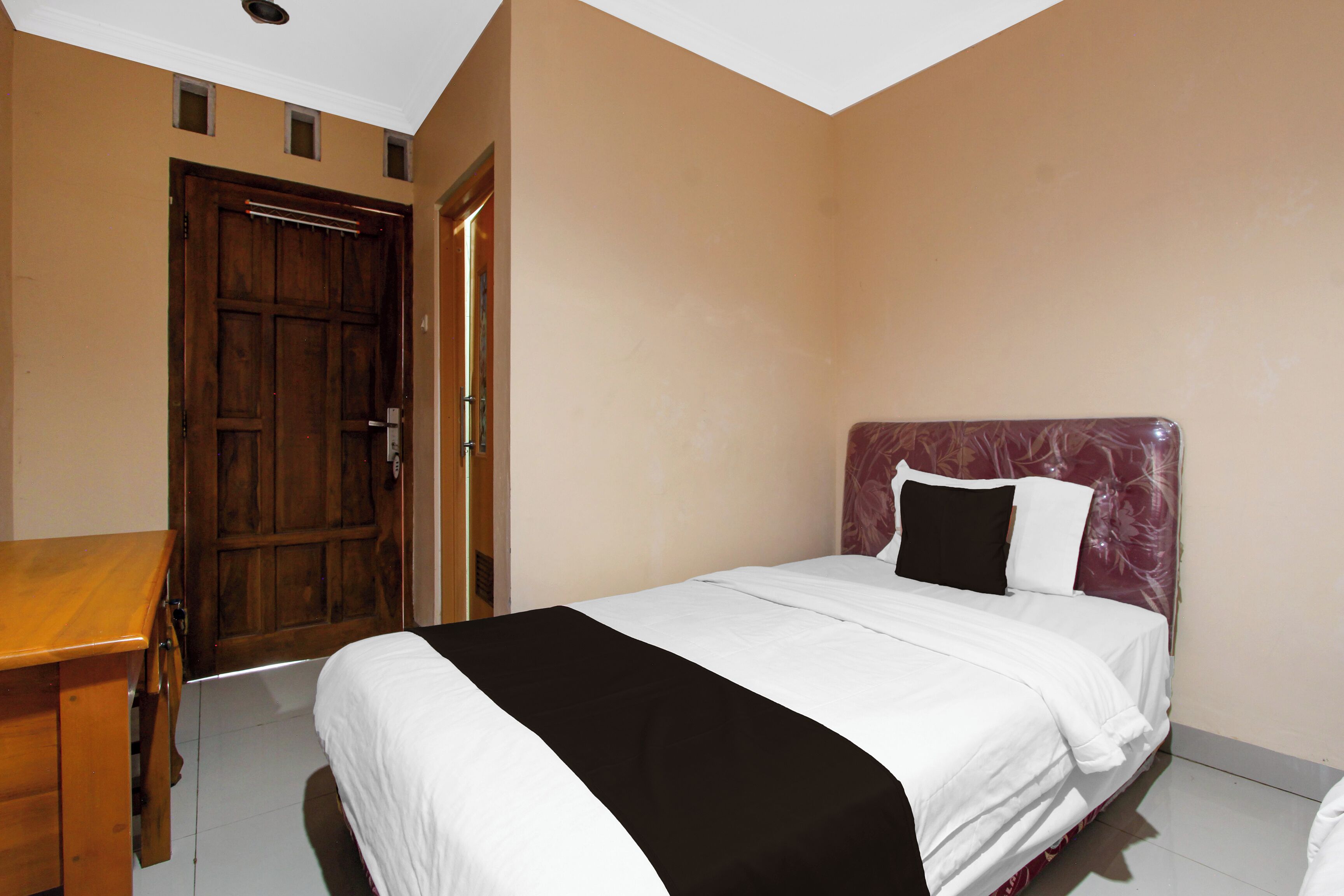 A bedroom with a wooden door, a bed with white and black bedding, and a wooden desk.