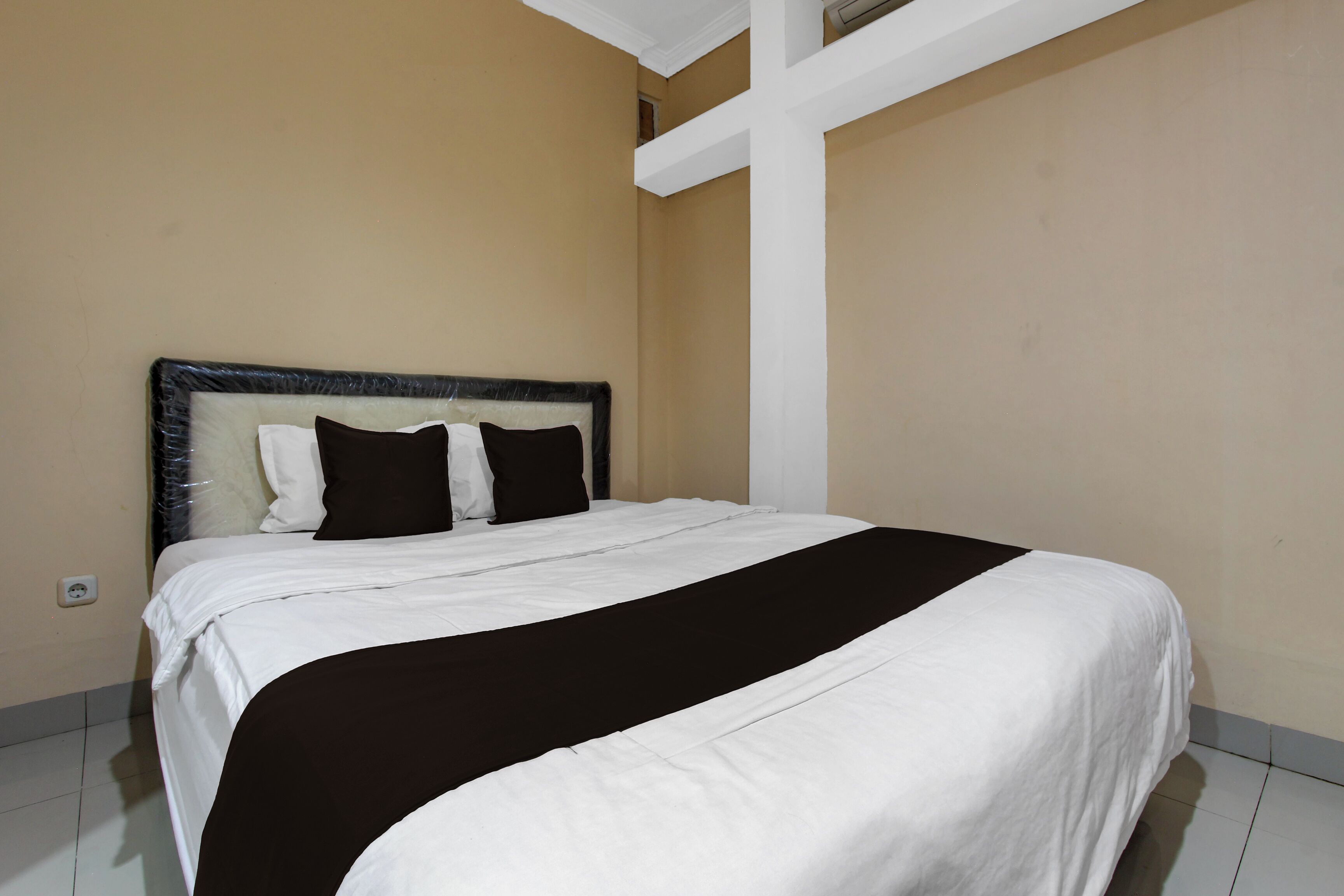 Un lit recouvert d’une couvre-lit noire et blanche, avec une tête de lit et une croix blanche au mur.