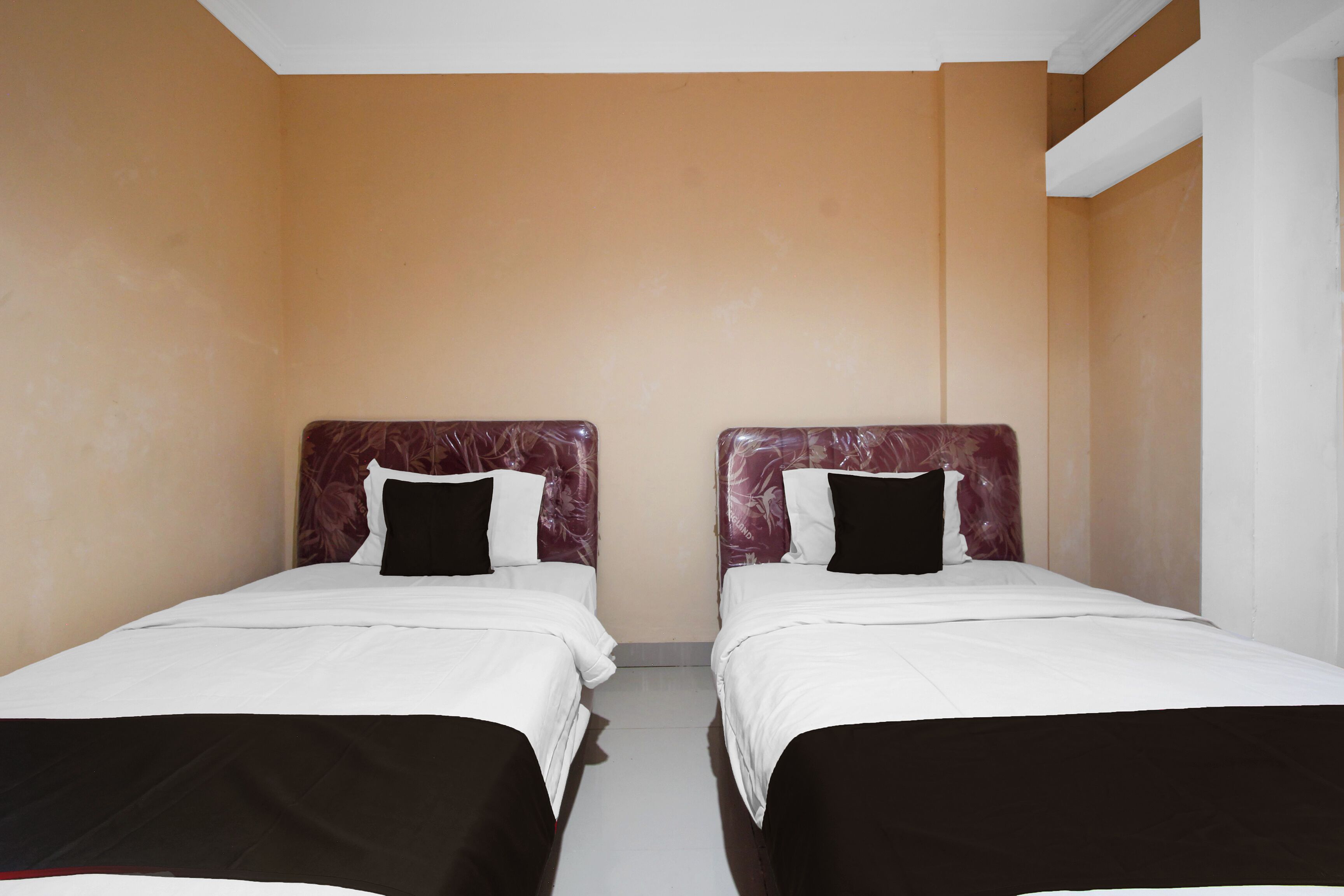 A room with two beds, each with a headboard, white bedding, and black pillows.