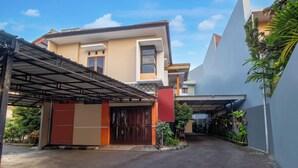 Een modern gebouw met een overdekte ingang, een hekwerk en plantenbakken langs het pad.