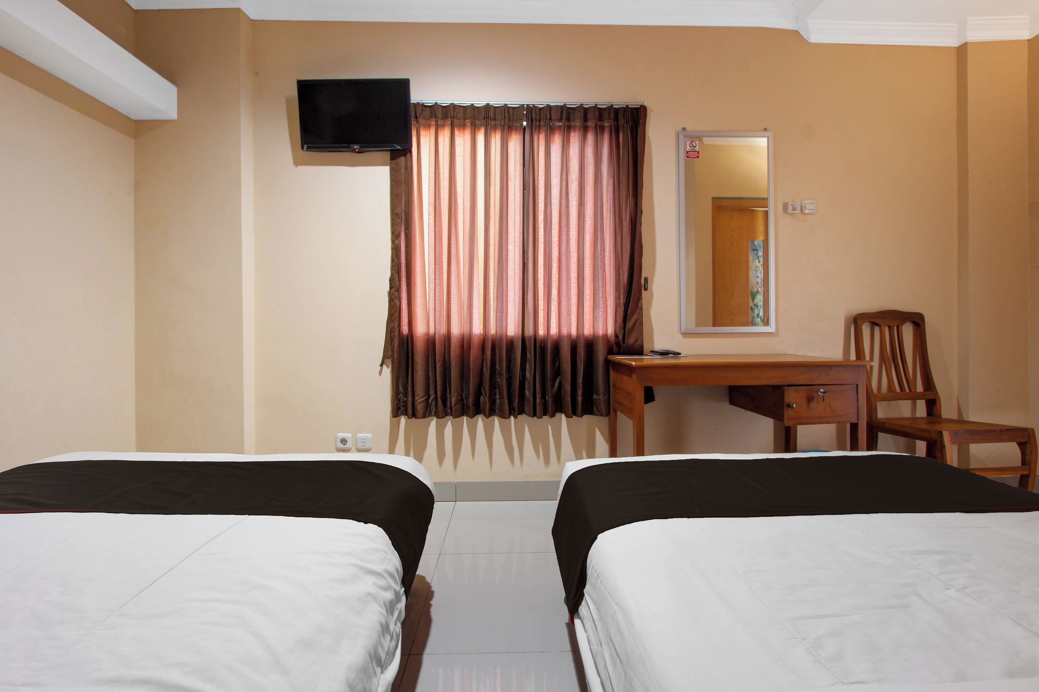Een hotelkamer met twee bedden, een bureau, een stoel, een televisie en een spiegel.