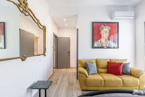 Un soggiorno moderno con un divano giallo, un tavolino, uno specchio grande e un quadro appeso al muro.