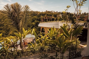 A building with a stone facade, arched windows, and a lush garden with various tropical plants. - Kanalla Boutique Hotel (Rembitan)