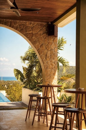 A covered outdoor seating area with stone walls, wooden furniture, and a view of the ocean. - Kanalla Boutique Hotel (Rembitan)