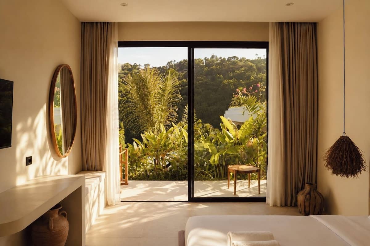 A bedroom with a large sliding glass door, a bed, a chair, a mirror, and a hanging light fixture.