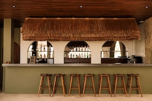 A bar area with a thatched ceiling, wooden stools, and a counter displaying various bottles. - Kanalla Boutique Hotel (Rembitan)