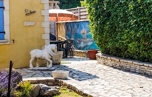A courtyard with a stone fountain, a white statue, a mural, and a yellow building. - Maison piscine proche Alpilles (Senas)