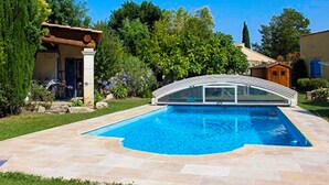 Una piscina con techo curvo, rodeada de un solado de piedra y abundante vegetación.
