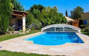 A swimming pool with a curved roof, surrounded by a stone deck and lush greenery. - Maison piscine proche Alpilles (Senas)