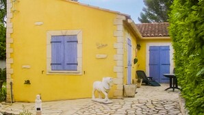 Un edificio amarillo con puerta azul, una pequeña estatua y un patio con baldosas de piedra.