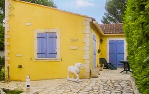A yellow building with a blue door, a small statue, and a stone-tiled patio. - Maison piscine proche Alpilles (Senas)