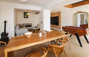 Ein Essbereich mit Holztisch und Stühlen, einer Couch, einem Fernseher und einem Kicker.