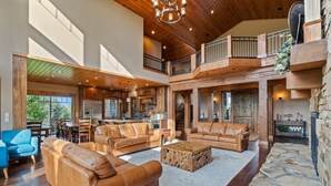A spacious living area with leather sofas, a stone fireplace, and a kitchen in the background. - Spring Shores Lodge | Luxury Mtn Estate, Sleeps 40, Private Lake & More! (Ashton)