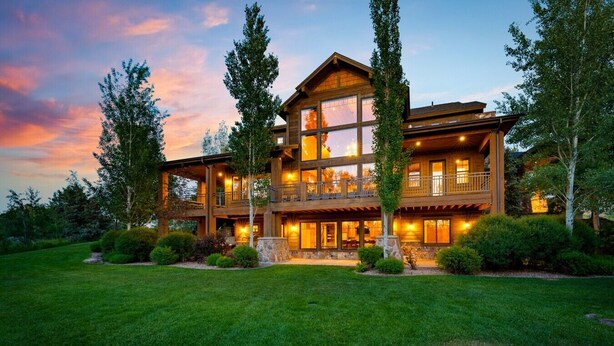 A large, multi-story wooden house with a balcony, surrounded by a well-maintained lawn and trees. - Spring Shores Lodge | Luxury Mtn Estate, Sleeps 40, Private Lake & More! (Ashton)
