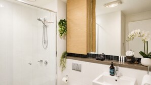 Un baño moderno con cabina de ducha de vidrio, un lavamanos blanco, un inodoro y un espejo sobre el lavamanos.