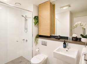 Ein modernes Badezimmer mit Duschkabine aus Glas, einem weißen Waschbecken, einer Toilette und einem Spiegel  über dem Waschbecken.