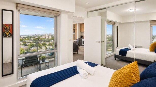 Habitación de hotel con una cama grande, balcón con vistas, zona de comedor separada y armario con espejo.