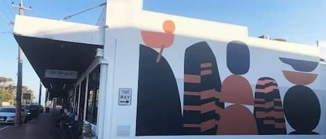 A building with a 'ONE WAY' sign, a covered entrance, and a mural with abstract figures.