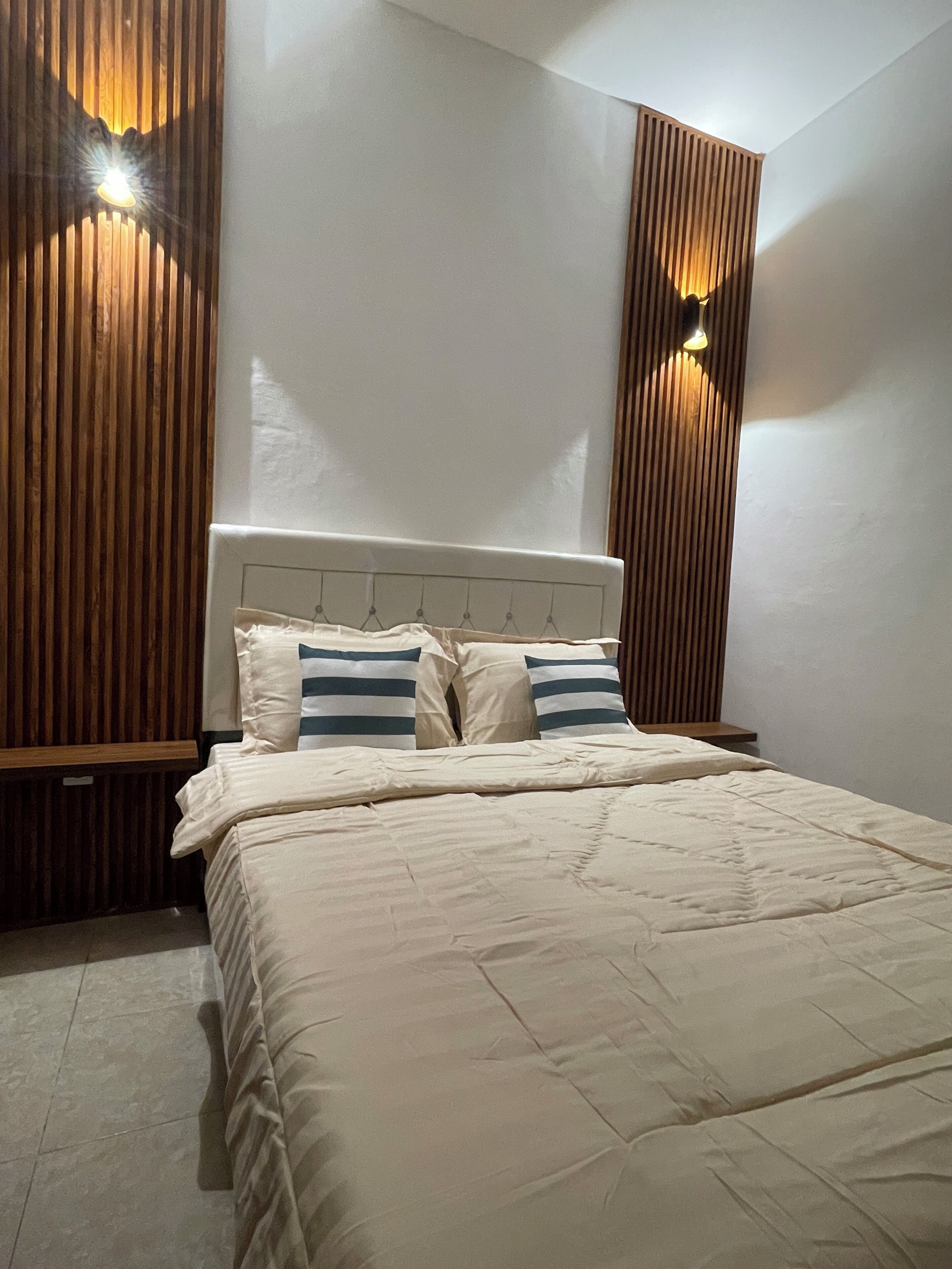 A bedroom with a bed, pillows, a headboard, wooden paneling, and wall-mounted lights.