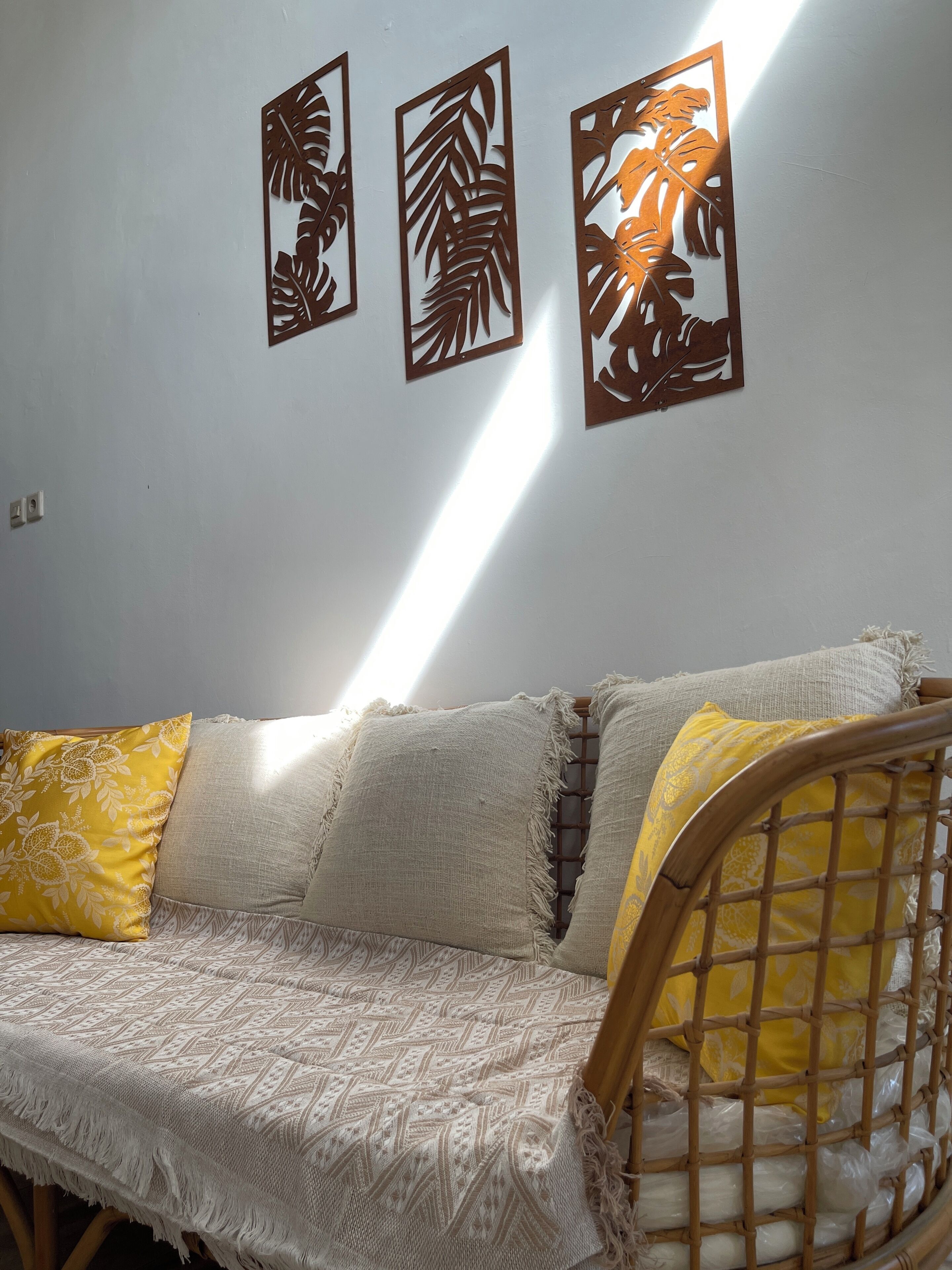 A room with a sofa, three wall art pieces, and a window casting light.