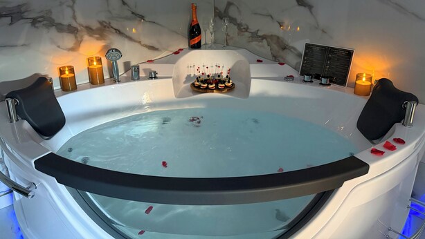 Ett bubbelbad med en vägg i marmor som bakgrund, ljus och en meny.