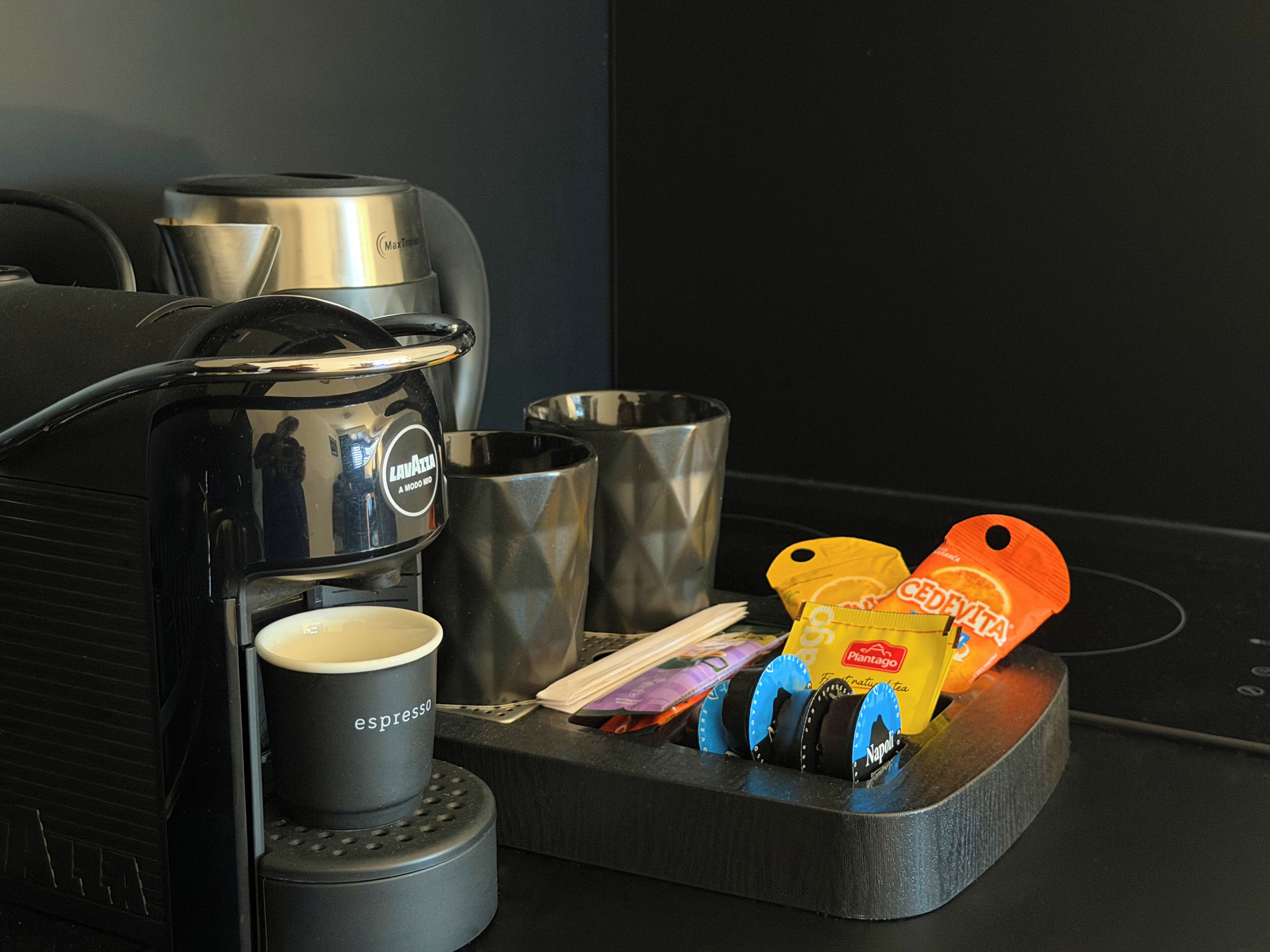 A coffee machine with a cup holder, a metal container, and a bag of coffee pods.
