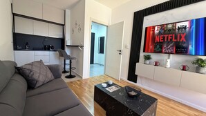 Ett modernt vardagsrum med en soffa, ett soffbord, en köksdel och en väggmonterad tv som visar Netflix.