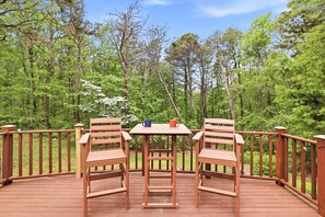 A wooden deck with two chairs and a table, surrounded by a wooden railing, overlooking a forested area. - Peaceful 2-bedroom house with AC in charming Dennis (Dennis)