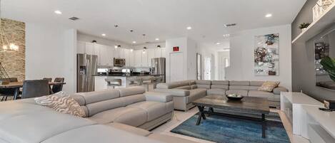 A modern living room with a sectional sofa, a coffee table, and a dining area with a chandelier.