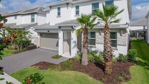 A modern two-story house with a garage, a well-maintained lawn, and two palm trees. - Mystical Dreams (Kissimmee)