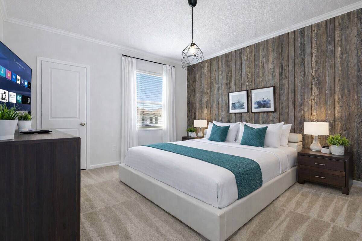 A bedroom with a bed, bedside tables, a desk, a television, and a window with curtains.
