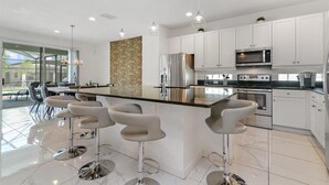 A modern kitchen with white cabinets, stainless steel appliances, and a central island with bar stools. - Mystical Dreams (Kissimmee)