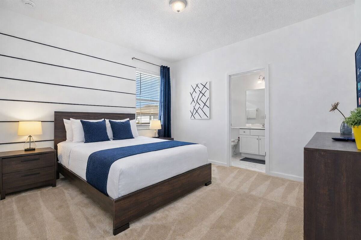 A modern bedroom with a large bed, bedside tables, a nightstand, a desk, a mirror, and a potted plant.