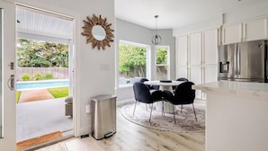 A modern kitchen with white cabinets, a stainless steel refrigerator, and a dining area with a round table and chairs. - Casa de Panda - 4-bedroom house with heated pool (Sacramento)