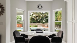 A dining area with a round table and four chairs, large windows, and a hanging light fixture. - Casa de Panda - 4-bedroom house with heated pool (Sacramento)