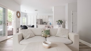 A modern living room with a sofa, a coffee table, and a kitchen in the background. - Casa de Panda - 4-bedroom house with heated pool (Sacramento)