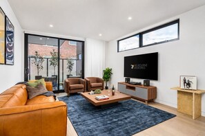 A modern living room with a leather sofa, two armchairs, a coffee table, and a flat-screen TV. - The Pavilion | Records, Space + MCG Moments Away! (Richmond)