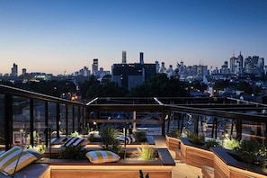 Eine Dachterrasse mit Sitzgelegenheiten, Blick auf die Stadtlandschaft und einem modernen architektonischen Design.